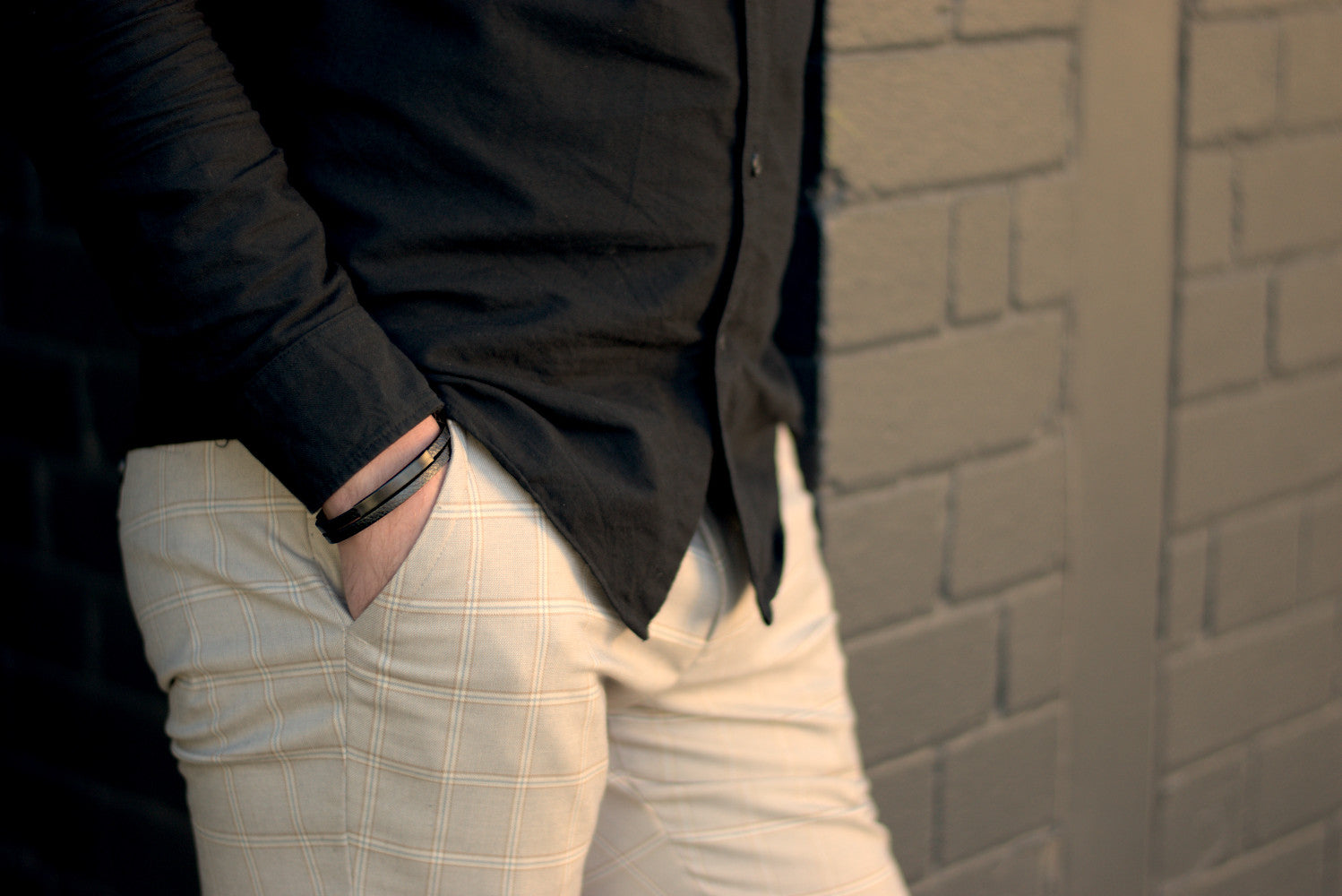 Well dressed man leaning against a wall wears a premium black leather bracelet from Rianrix Accessories 